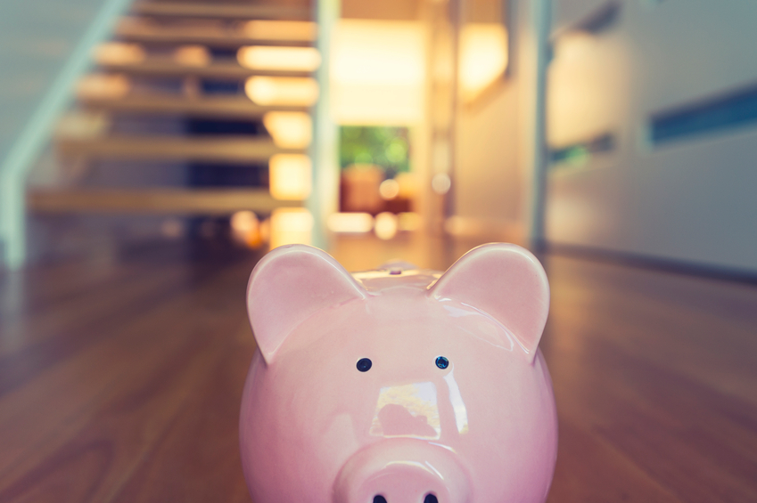 Saving for a home concept. Piggy bank standing at front door with house interior in the background. Pig is pink in foreground and house is modern style. Copy space.